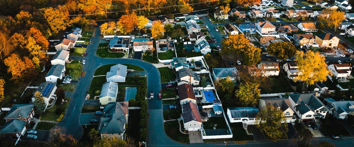 An aerial view of a residential area with houses, roads, and autumn-colored trees.