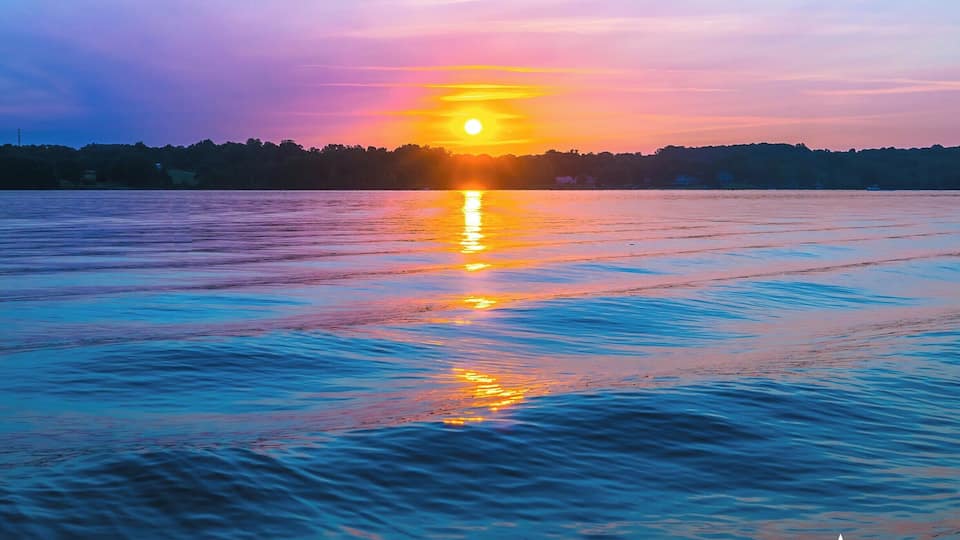 A sunset over a calm body of water with a silhouette of trees in the background.