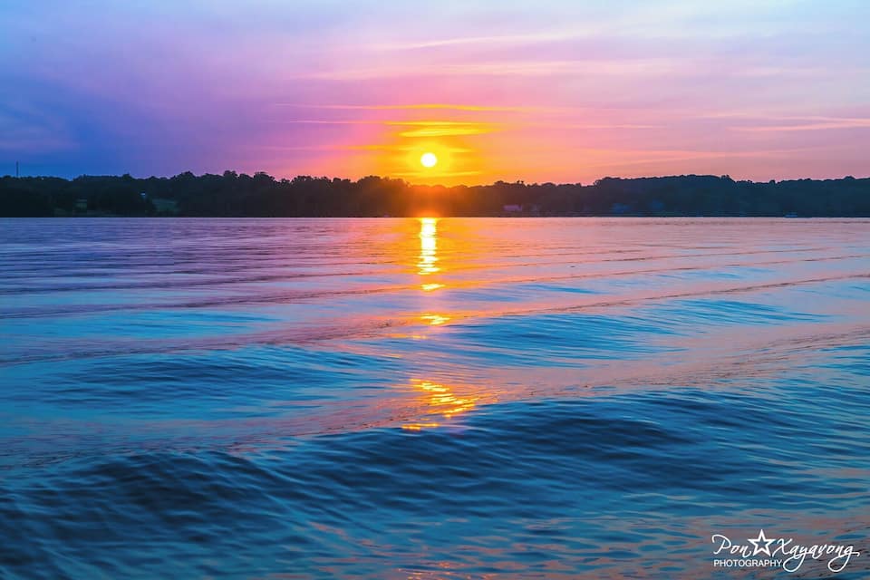 A sunset over a calm body of water with a silhouette of trees in the background.