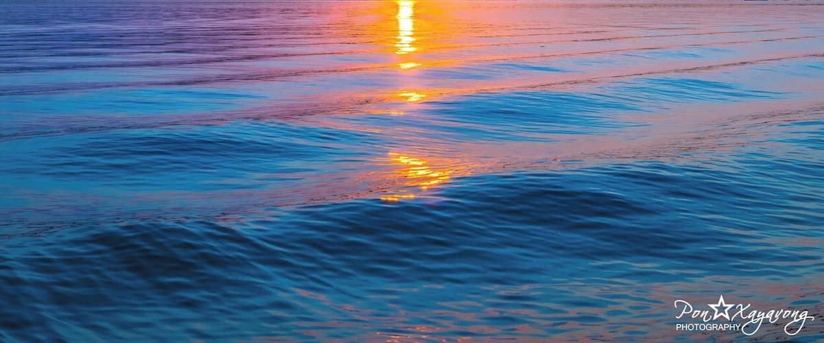 A sunset over a calm body of water with a silhouette of trees in the background.