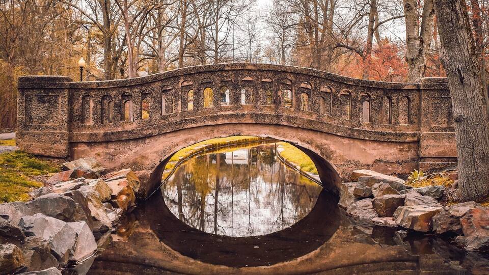 A stone bridge over a circular pond with trees in the background.