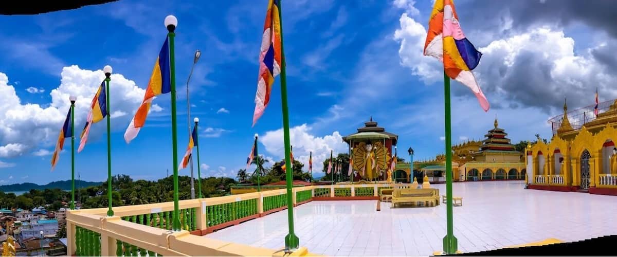 A golden pagoda, a green-roofed pavilion, and colorful flags against a blue sky.
