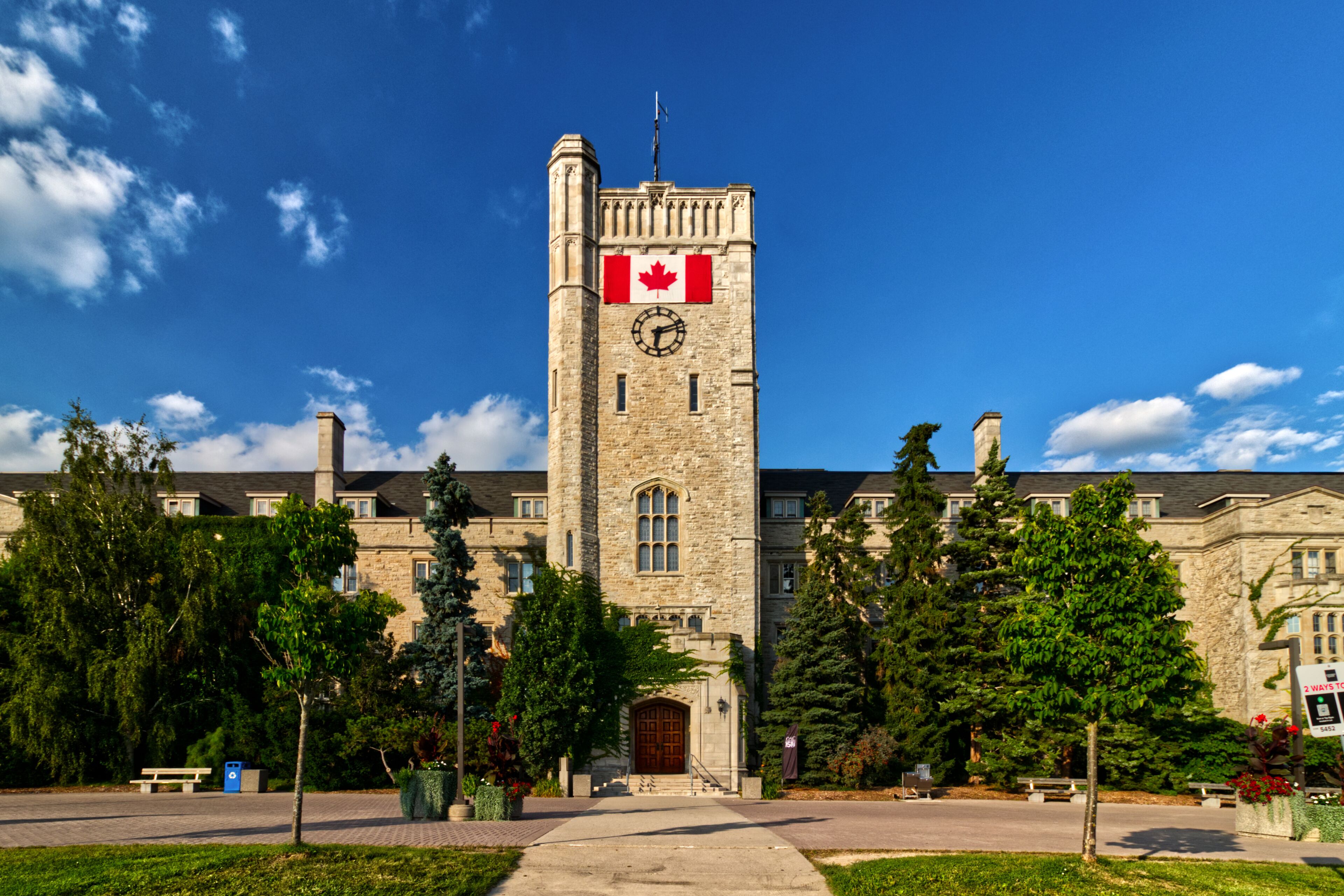 A stone building with a clock tower, a red maple leaf flag, and a clear blue sky.