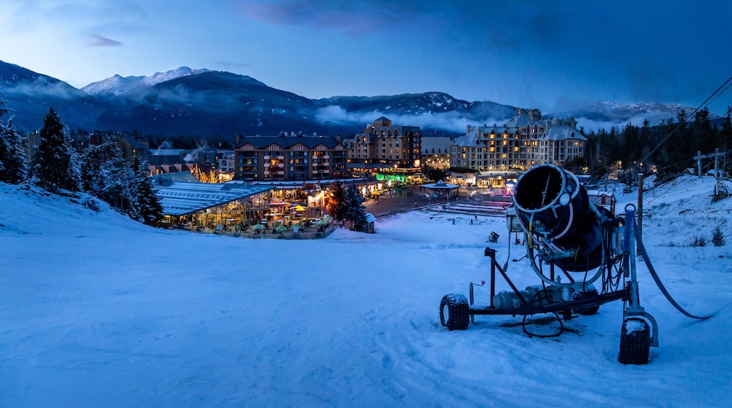 Une station de montagne enneigée au crépuscule, avec des bâtiments illuminés et un télésiège.