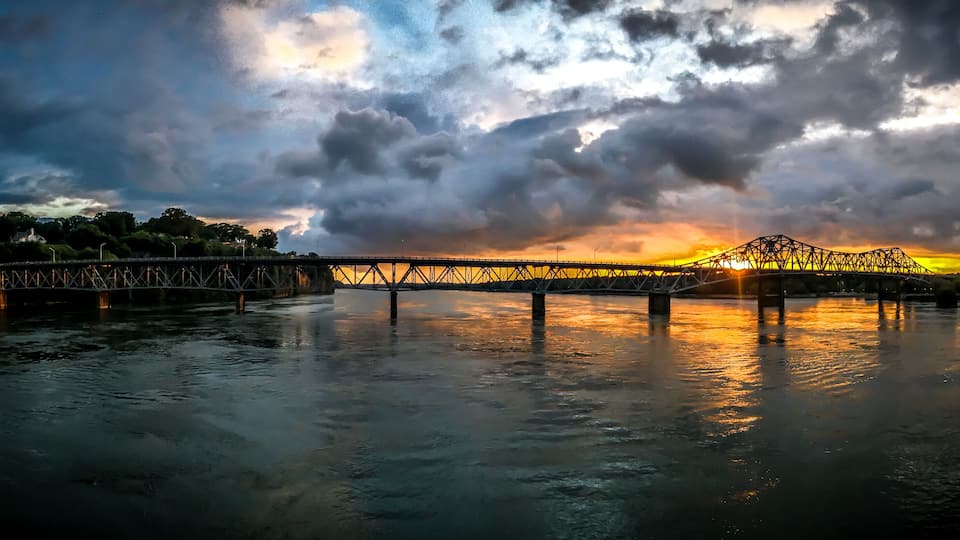 A bridge over a river with a sunset in the background.