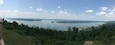 Ein See, umgeben von dichtem Wald und fernen Hügeln.