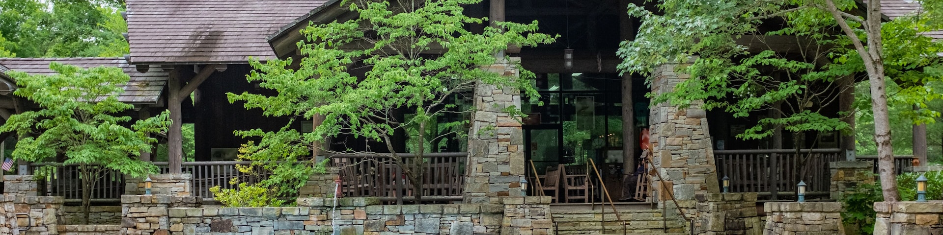 A rustic lodge with stone pillars and a covered porch, surrounded by lush greenery.