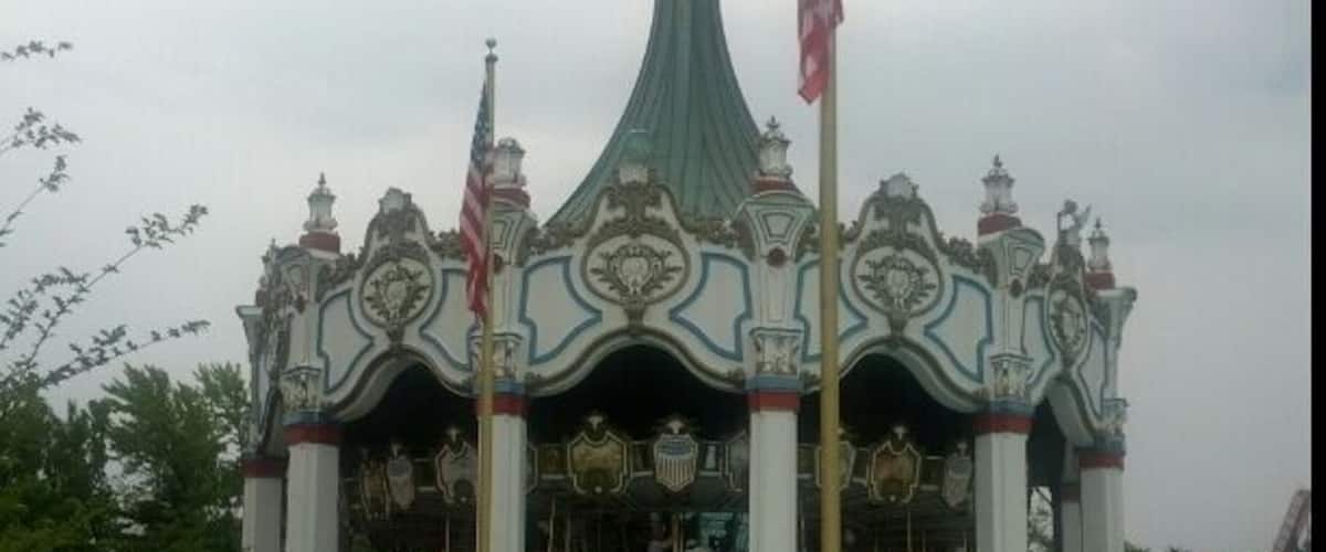 A carousel with ornate decorations and flags, surrounded by a flower bed.