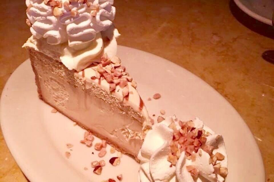 A slice of cheesecake on a plate with whipped cream and chopped nuts on top.