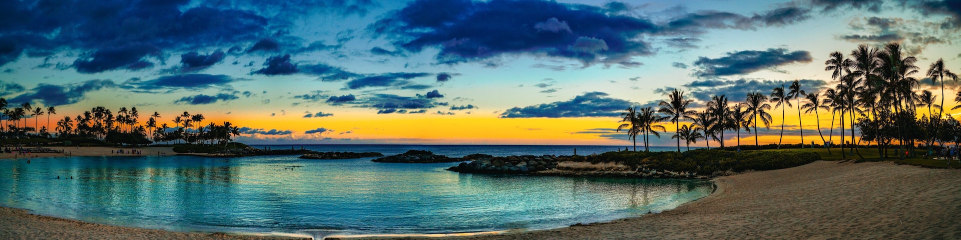 A beach with palm trees, calm water, and a sunset sky.