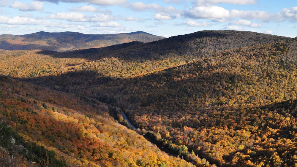 Une vallée aux couleurs automnales, une route sinueuse et des collines lointaines.
