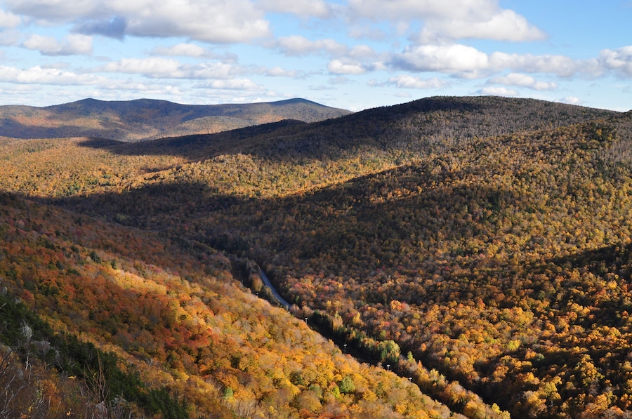 Une vallée aux couleurs automnales, une route sinueuse et des collines lointaines.