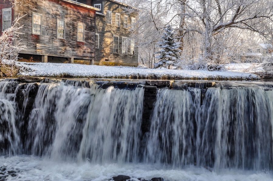 Una cascada en un paisaje nevado con un edificio de madera al fondo.