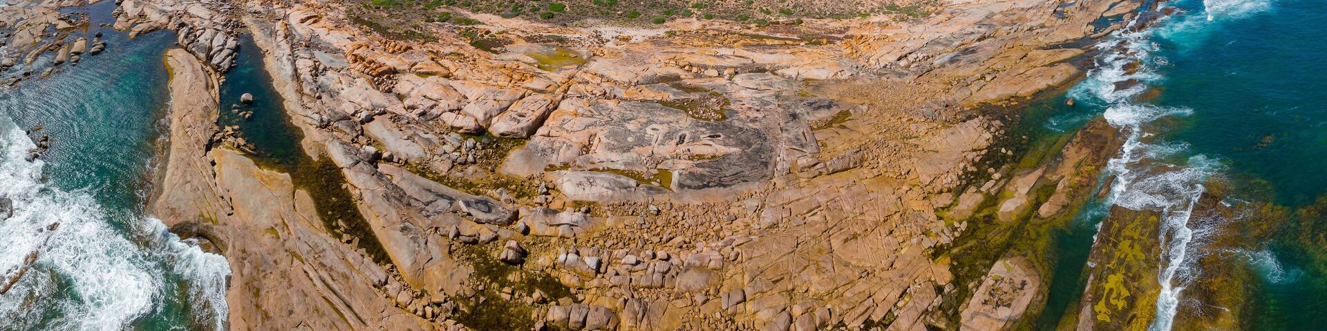 Aerial panorama view of a wide coastal rock ledge below a rugged plateau with ocean all around