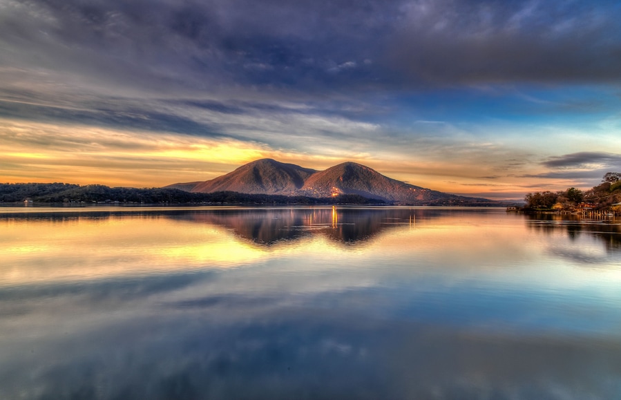 Ein Bergpanorama spiegelt sich in einem stillen See unter einem Sonnenuntergangshimmel.