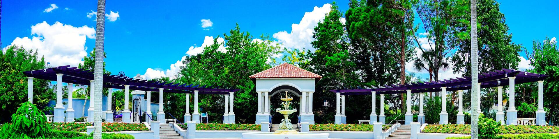 A garden with a central fountain, surrounded by white columns and covered walkways.