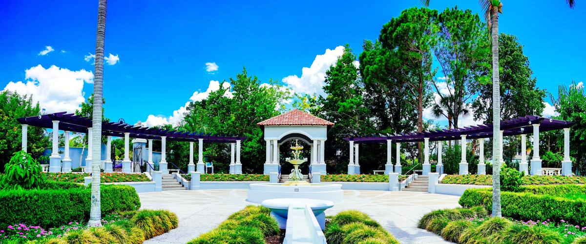 A garden with a central fountain, surrounded by white columns and covered walkways.