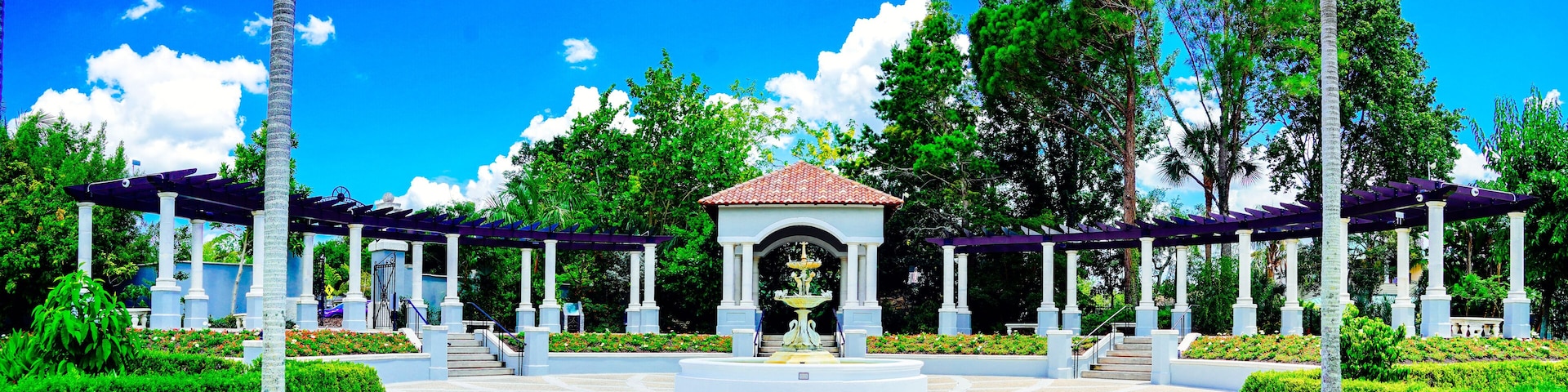 A garden with a central fountain, surrounded by white columns and covered walkways.