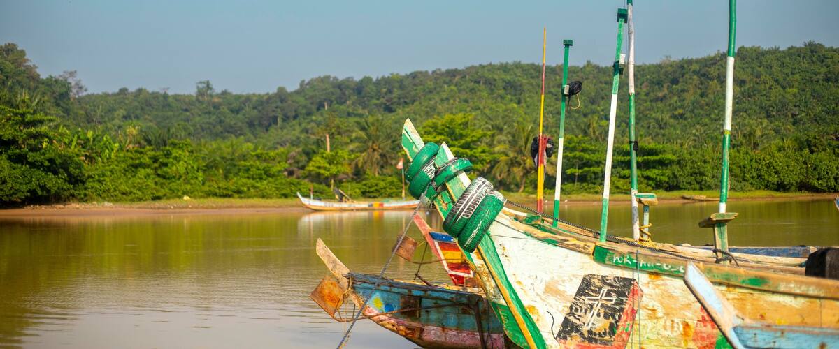 A river with a boat and flags, surrounded by lush greenery.