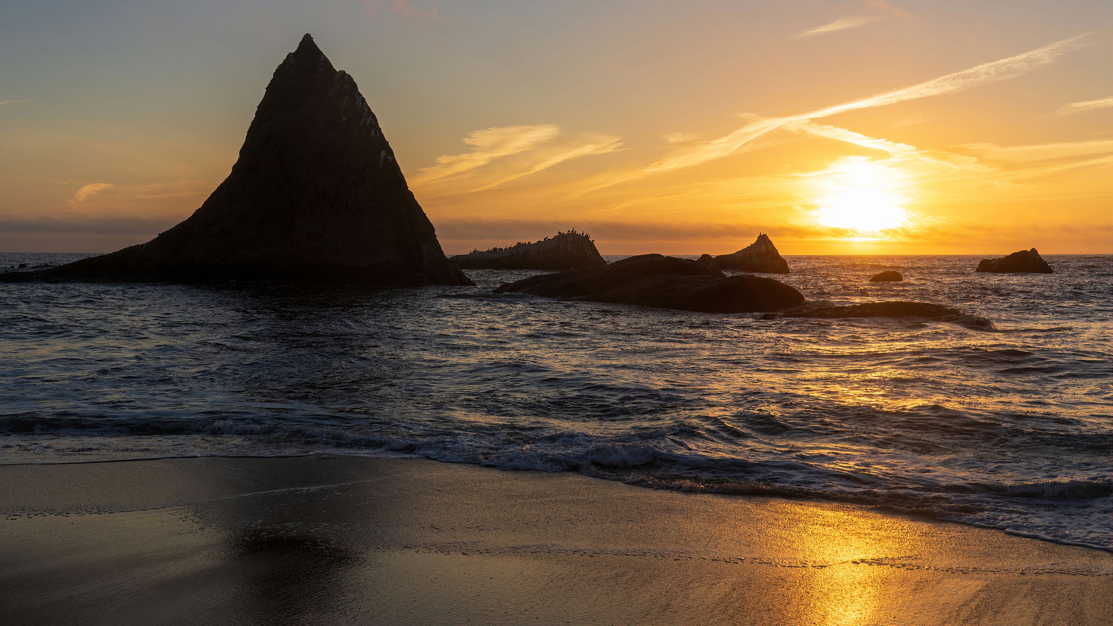 A coastal sunset with a prominent rock formation silhouetted against the sky.