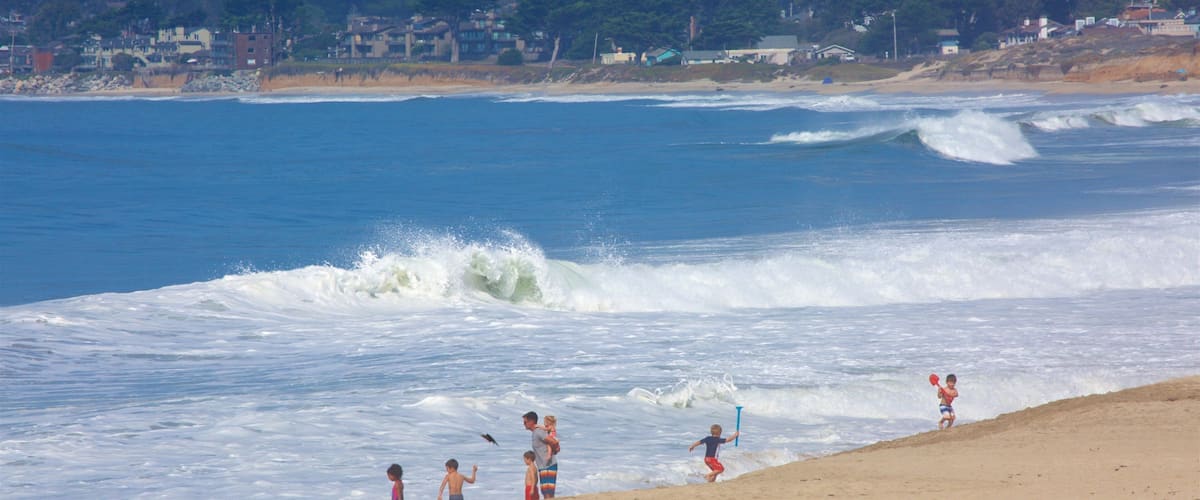 A beach with waves, people, and houses in the background.
