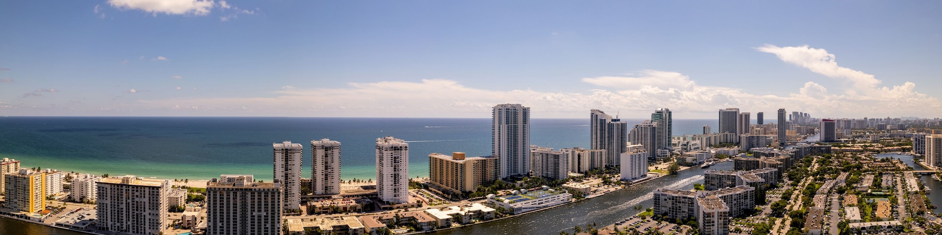 A coastal cityscape with high-rise buildings, a river, and a clear blue sky.