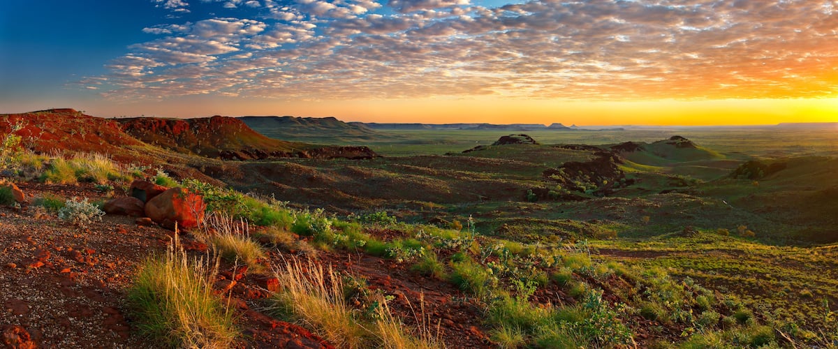 A vast landscape with rolling hills, sparse vegetation, and a dramatic sunset sky.