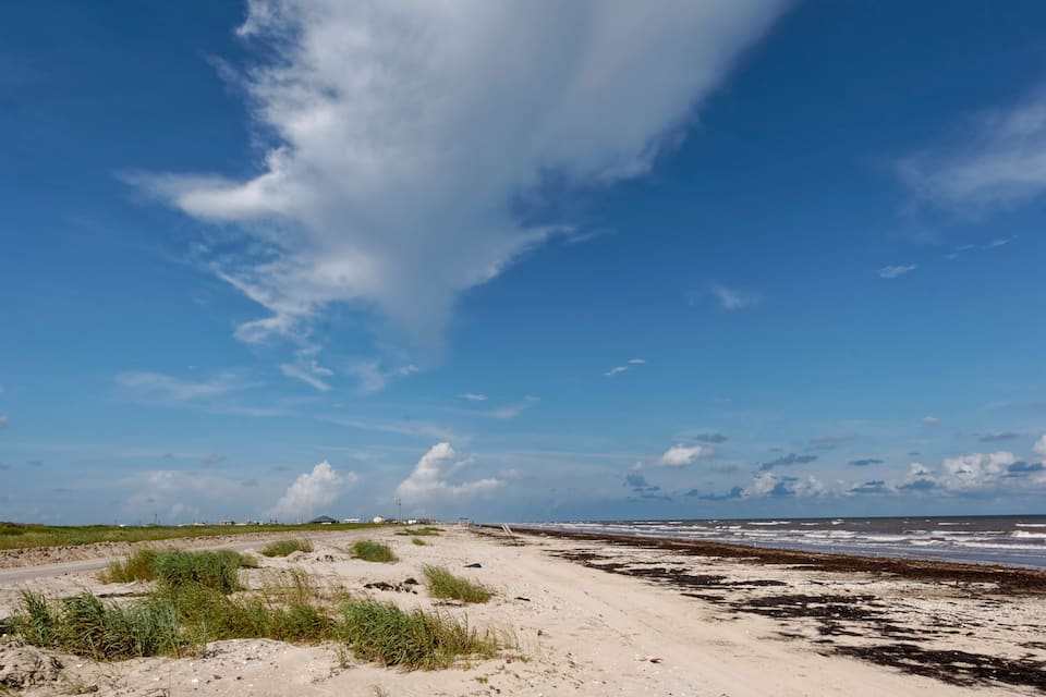En sandstrand med sparsom beplantning og en klar blå himmel med spredte skyer.