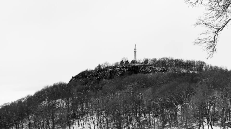 A snow-covered hill with a tower on top, surrounded by leafless trees.