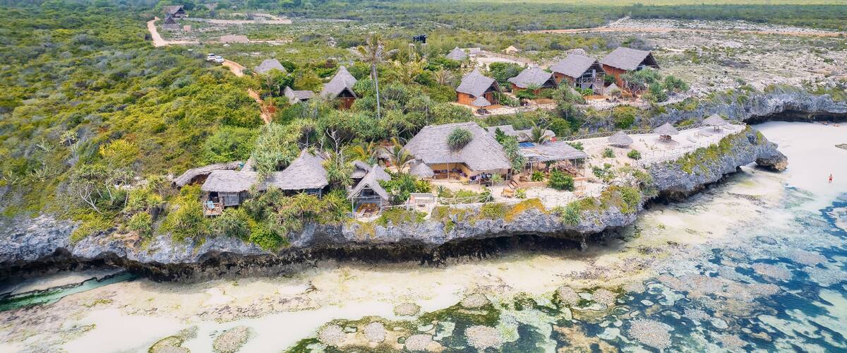 A coastal village with thatched-roof houses surrounded by lush greenery and a clear blue sea.