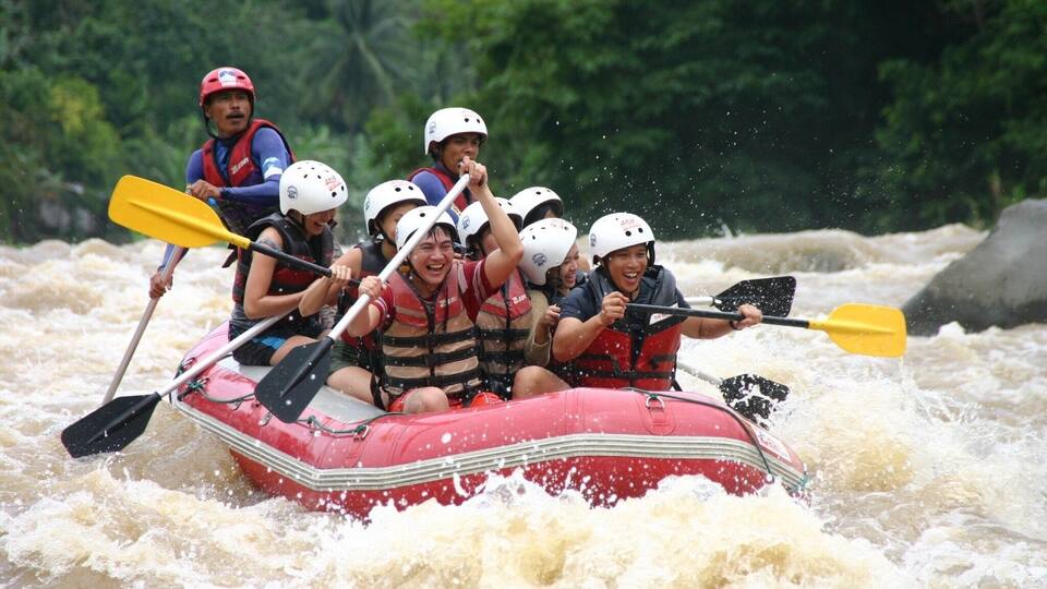 A group of people in a red inflatable raft navigating through whitewater rapids.
