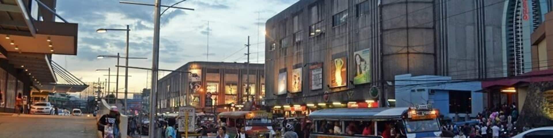 A busy street with a large building labeled 'GAISANO' and a bus in the foreground.