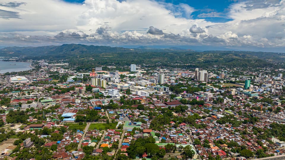 A cityscape with a mix of residential and commercial buildings, a river, and mountains in the background.