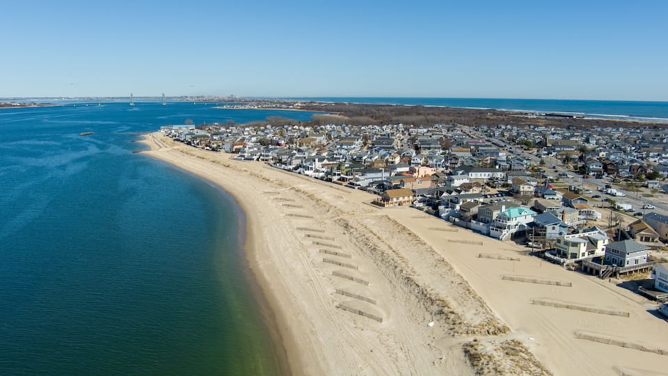 A coastal town with a beach, houses, and a bridge in the distance.
