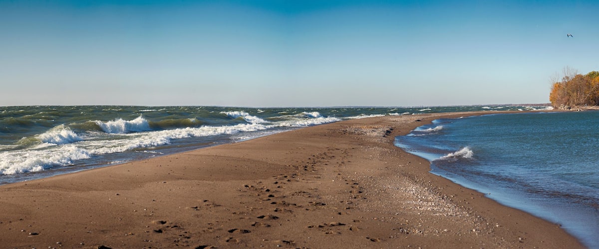 A beach with waves, a sandy shore, and a forested island in the distance.
