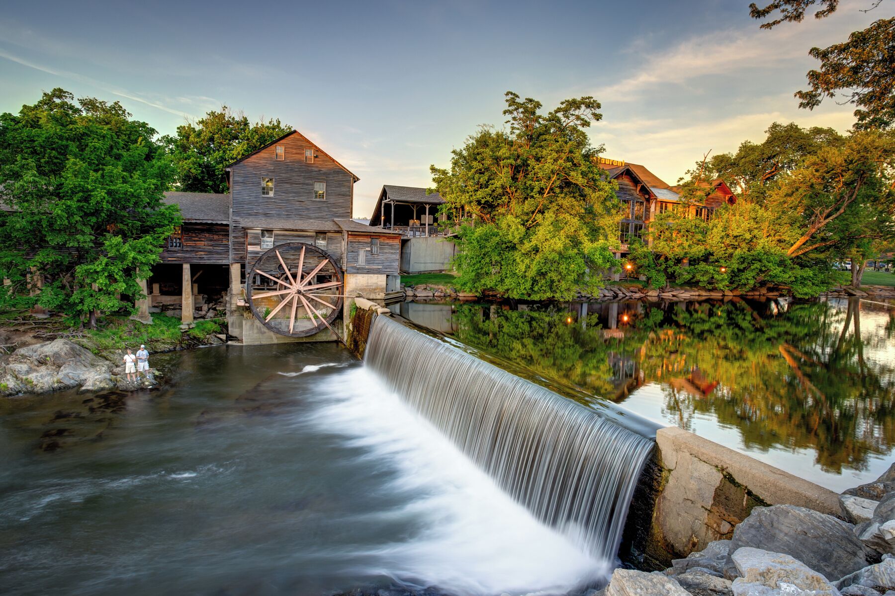 A water mill with a large wheel, a wooden house, and a waterfall.
