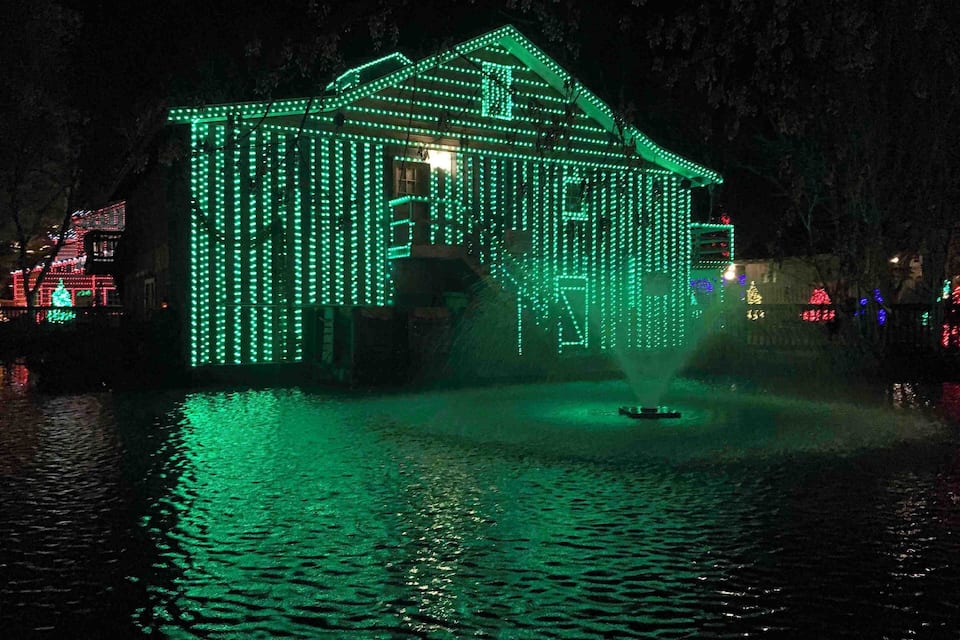 A house illuminated with green lights, surrounded by water and reflections.