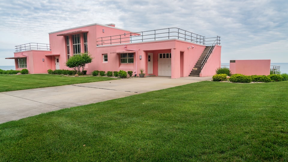 A pink house with a white door, a small tree, and a clear sky.