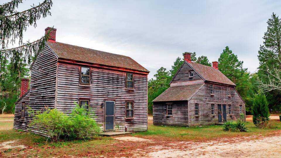 Two wooden houses with red brick chimneys, surrounded by grass and trees.