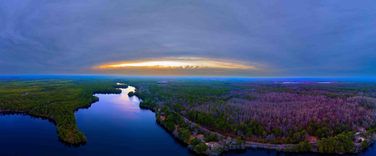 A river winding through a forested landscape with a sunset in the distance.
