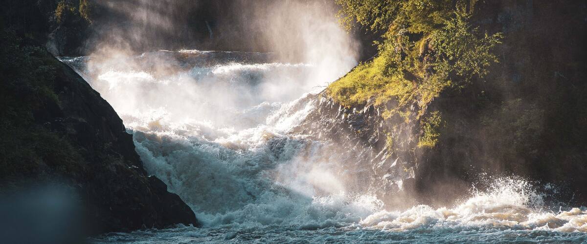 A turbulent river with a waterfall, surrounded by rocky terrain and greenery.