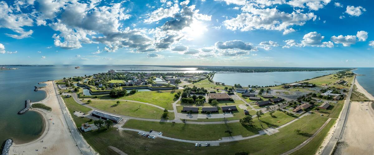 An aerial view of a coastal military base with a beach, green fields, and a large body of water.