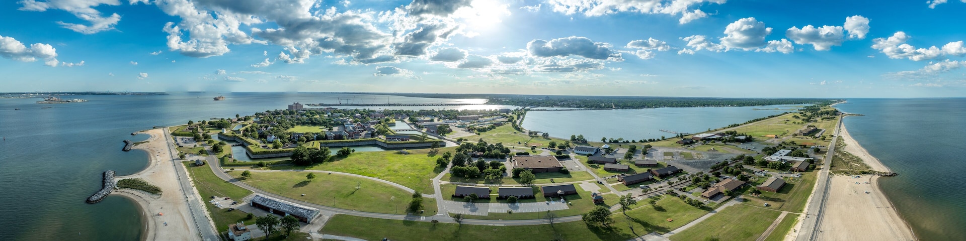 An aerial view of a coastal military base with a beach, green fields, and a large body of water.