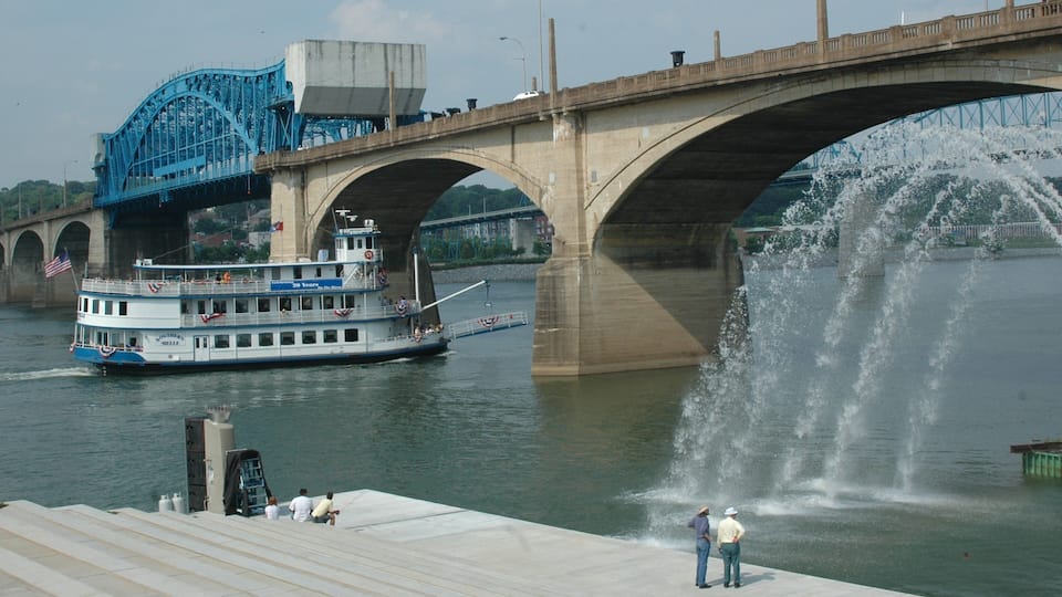 A river with a boat, a bridge, and a fountain.