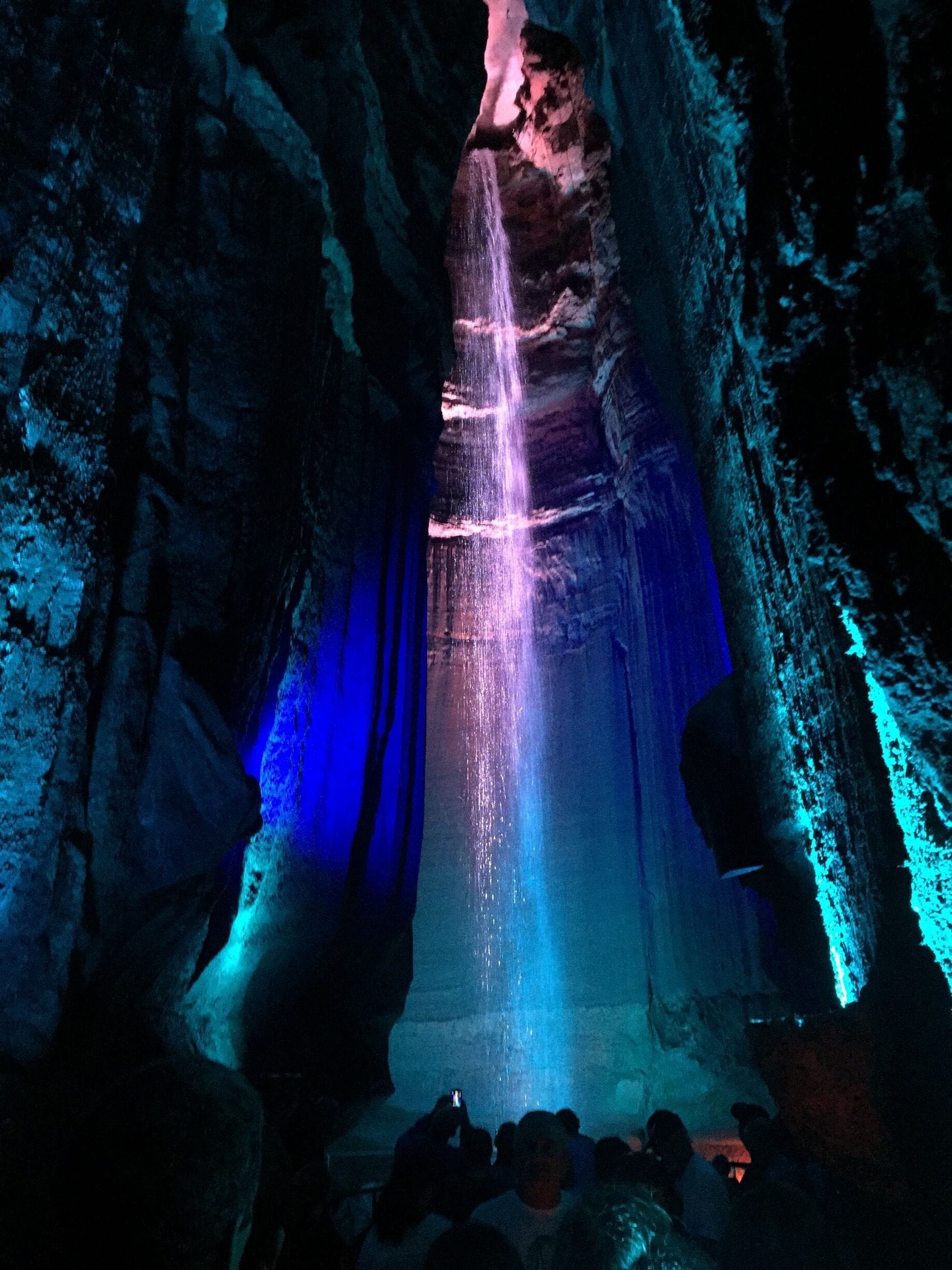 A cave with a waterfall illuminated by blue and pink lights.