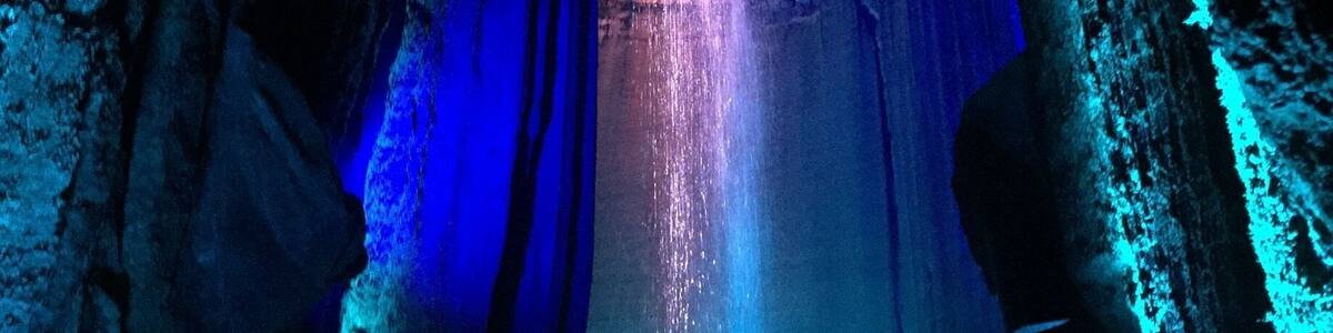 A cave with a waterfall illuminated by blue and pink lights.