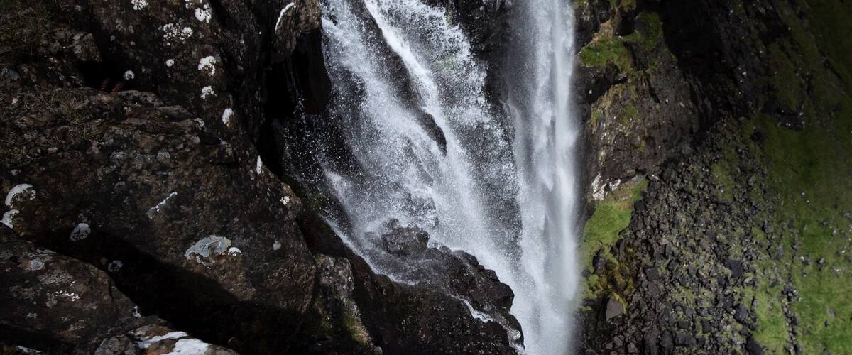 A waterfall cascading over dark rocks with patches of snow.