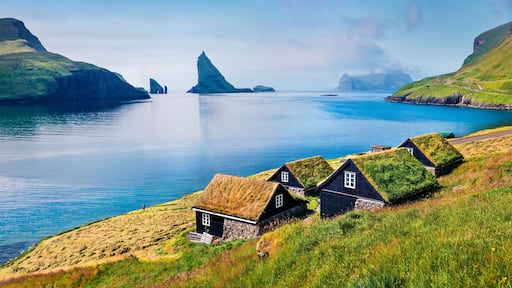 En kystlandsby med traditionelle huse, en fjord og en markant klippe.