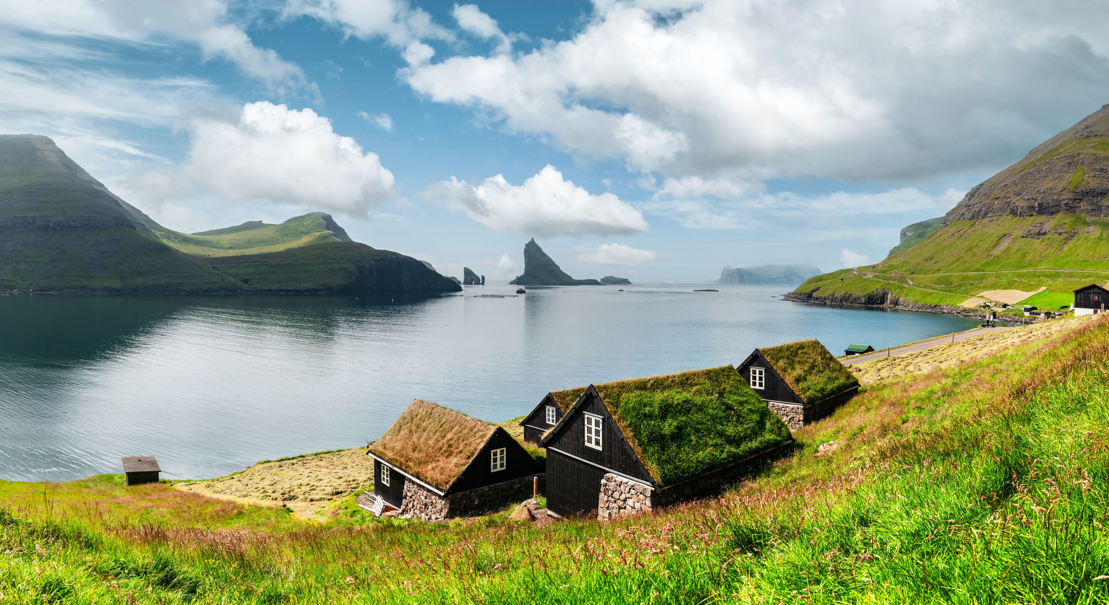 A coastal landscape with a body of water, grassy hills, and traditional black houses with thatched roofs.