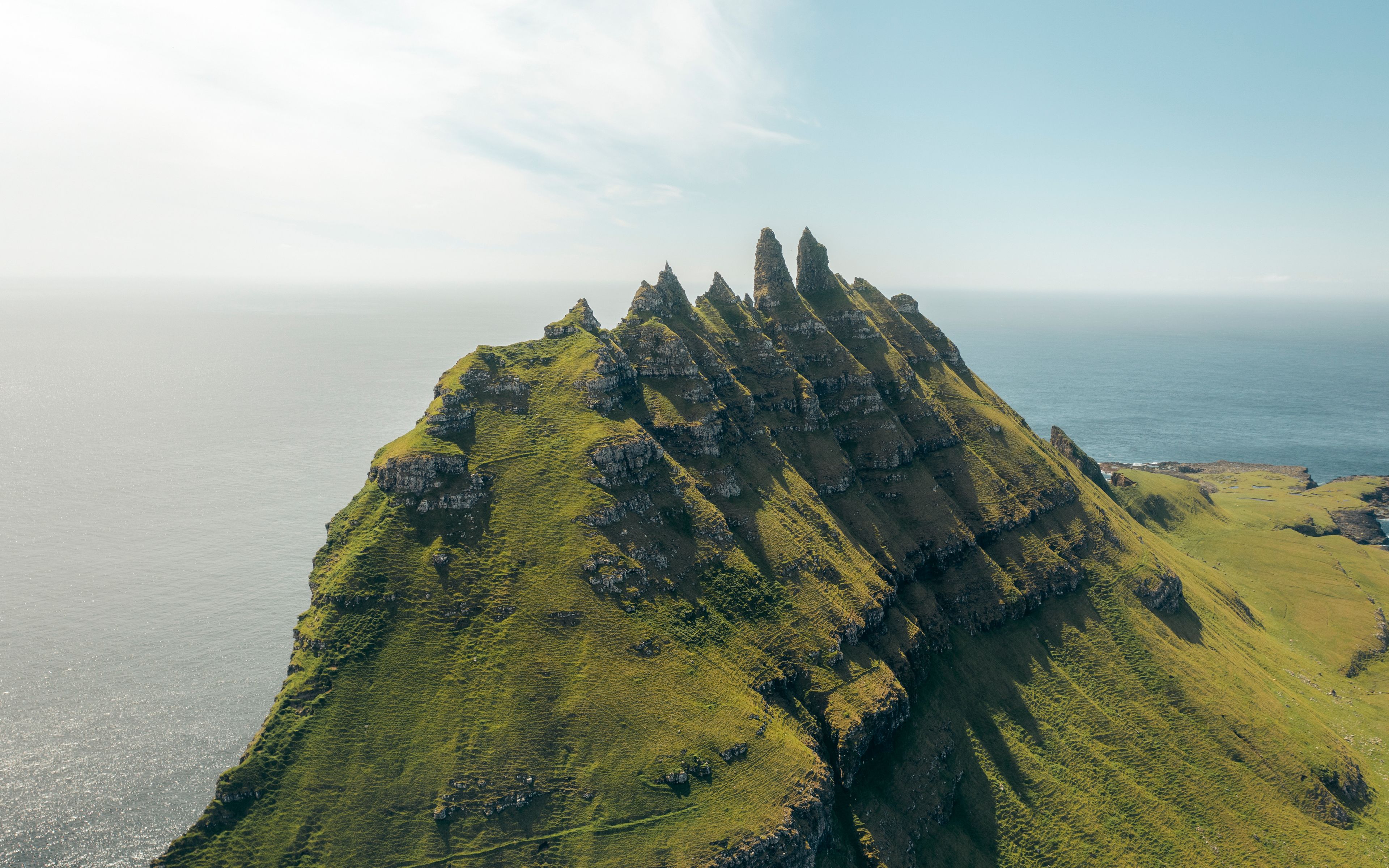 A rugged, green-clad mountain with sharp peaks and a coastline in the background.